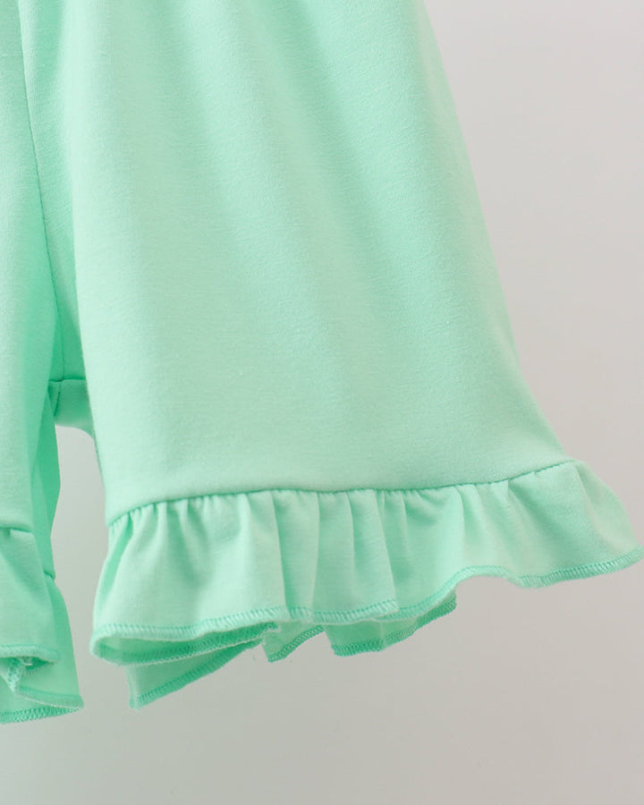 Close-up of a light green long-sleeve top with ruffled hem on a plain background