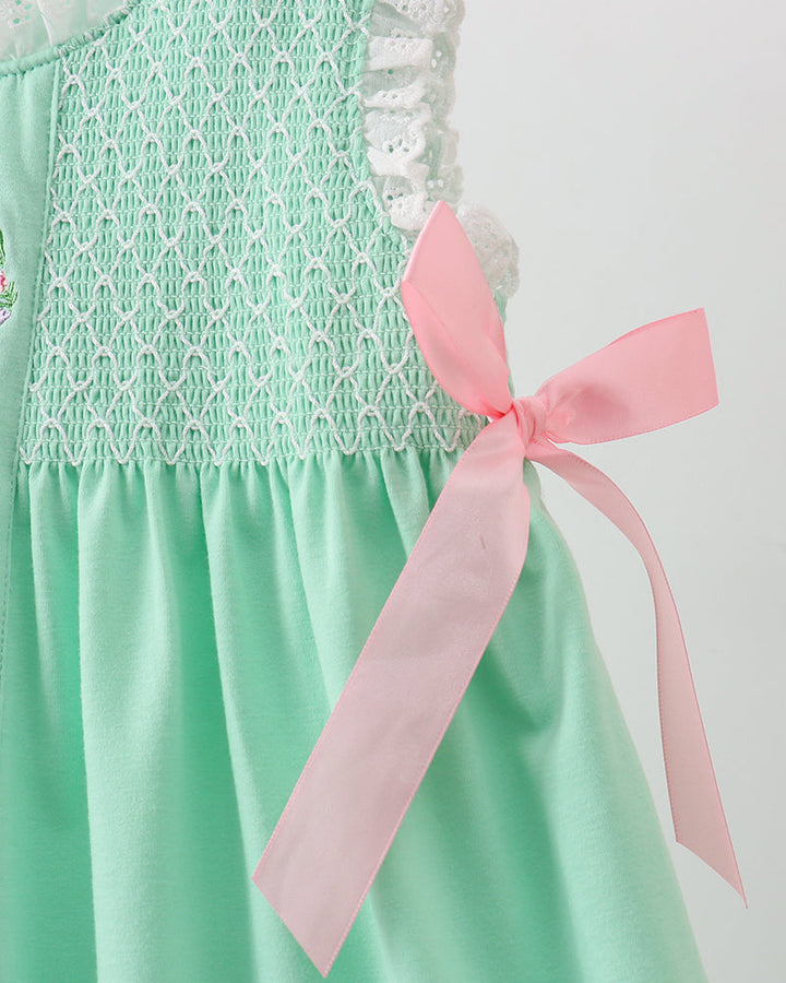 Green dress with white lace details and a pink ribbon on a plain background