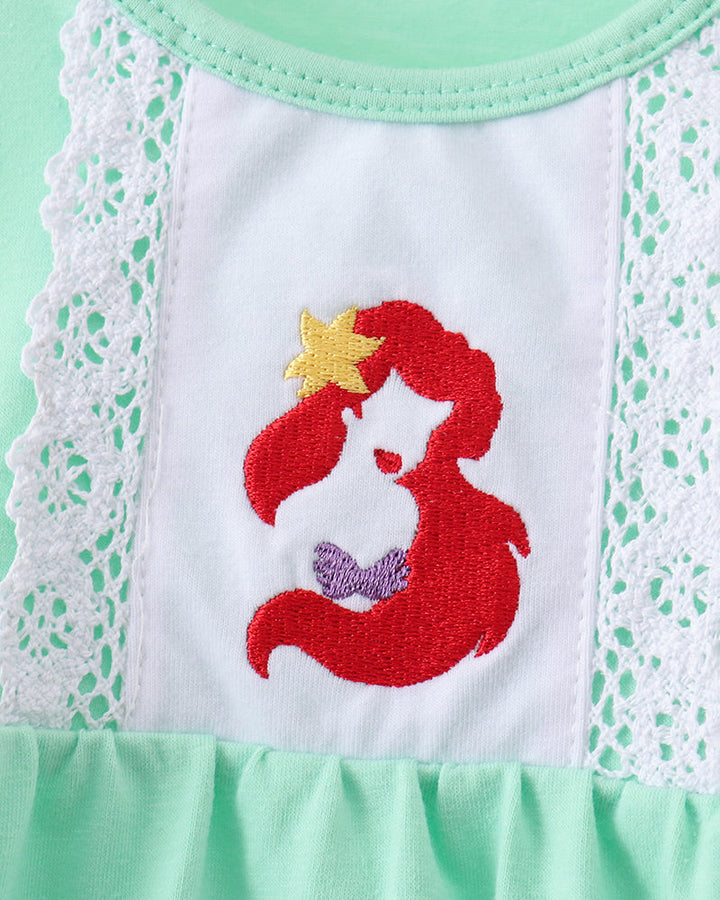 Close-up of a mint green and white baby dress featuring an embroidered mermaid design with a yellow starfish on the chest, bordered by white lace.