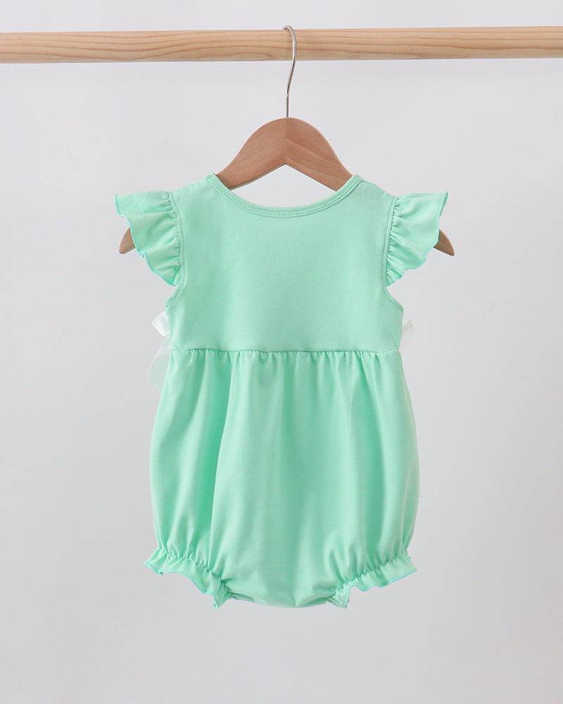 A mint green baby romper with ruffled cap sleeves and a gathered waist, hanging on a wooden hanger from a light wood rod against a plain light gray background.