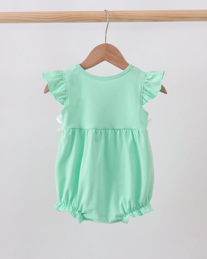 A mint green baby romper with ruffled cap sleeves and a gathered waist, hanging on a wooden hanger from a light wood rod against a plain light gray background.