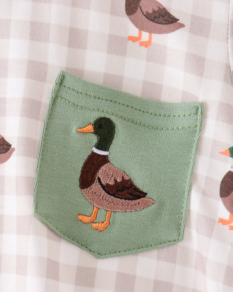 Close-up of a baby garment featuring a sage green front pocket with an embroidered duck design, set against a beige and white gingham pattern with scattered duck motifs.