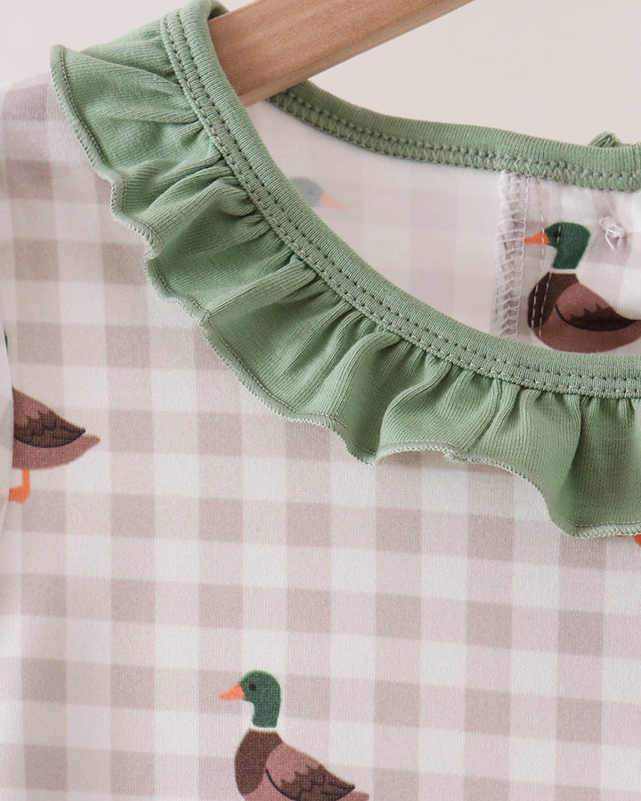 Close-up of a baby top with a sage green ruffled collar, a beige and white gingham pattern, and printed ducks, hanging on a wooden hanger.