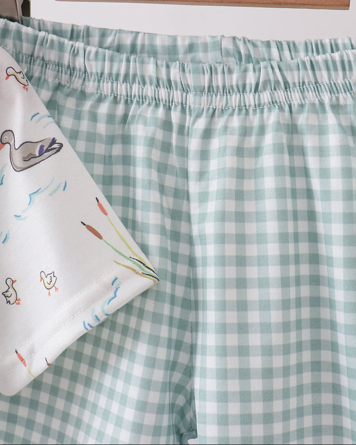 Green and white checkered shorts on a wooden hanger with a colorful pouch underneath.