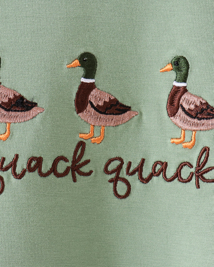 Close-up of a sage green embroidered fabric featuring three mallard ducks and the word &