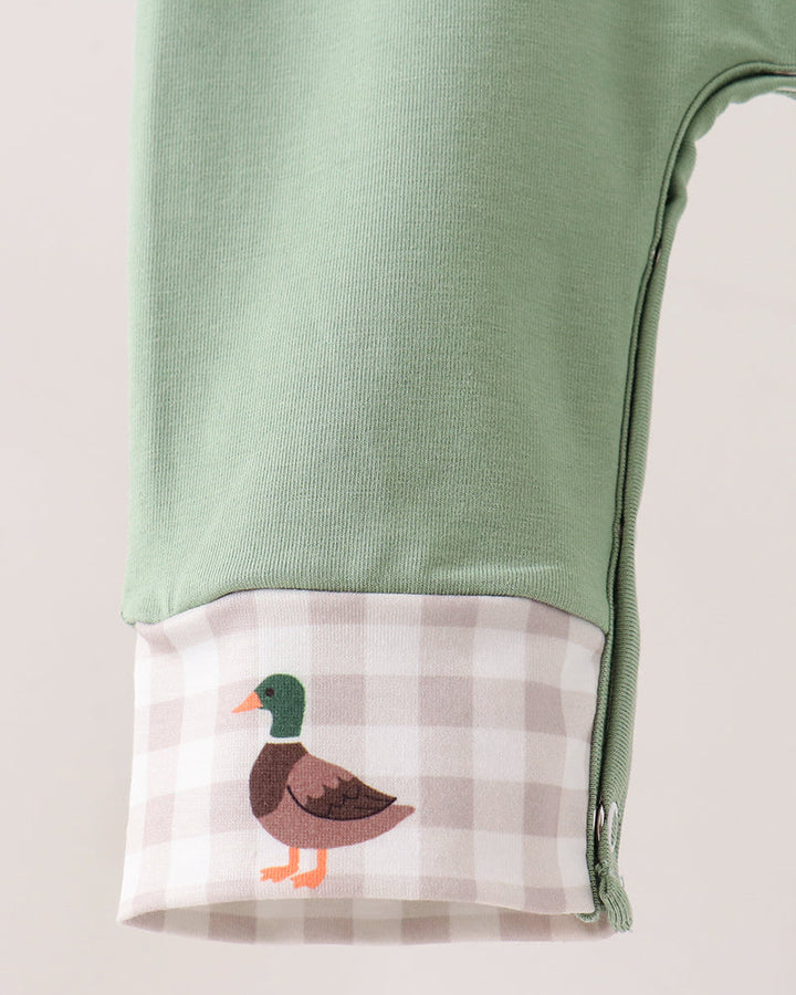 A close-up of a sage green garment, likely a baby romper or pants leg, featuring a gingham cuff with a cartoon mallard duck illustration.