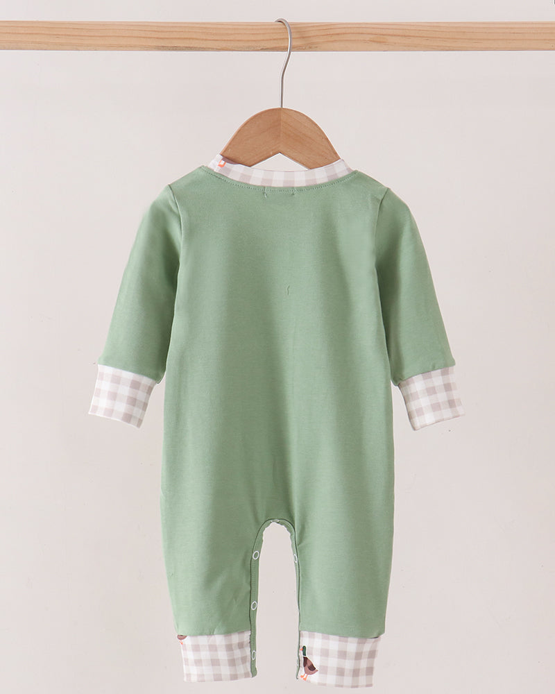 A baby long-sleeve footless jumpsuit in sage green, hanging on a wooden hanger. The jumpsuit features a white and pink gingham check patterned collar and cuffs, shown against a plain light beige background.