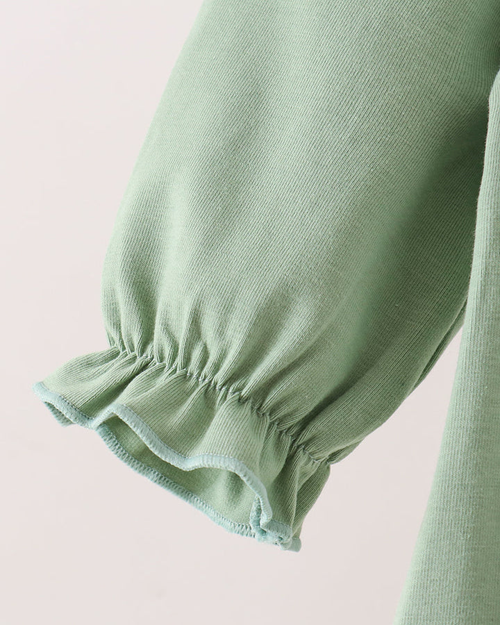 Close-up of a sage green knit garment sleeve with a gathered ruffled cuff, shown against a plain light background.