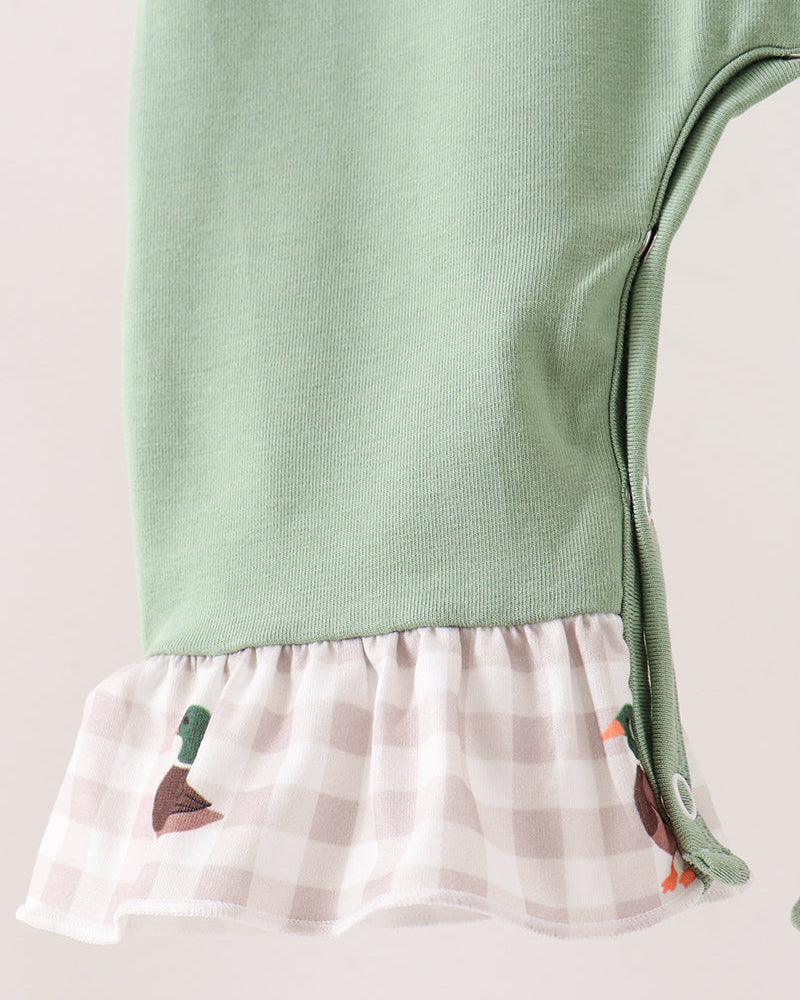Close-up of a baby garment with a sage green upper section and a ruffled hem made of white and pale pink gingham fabric with small duck and carrot motifs.