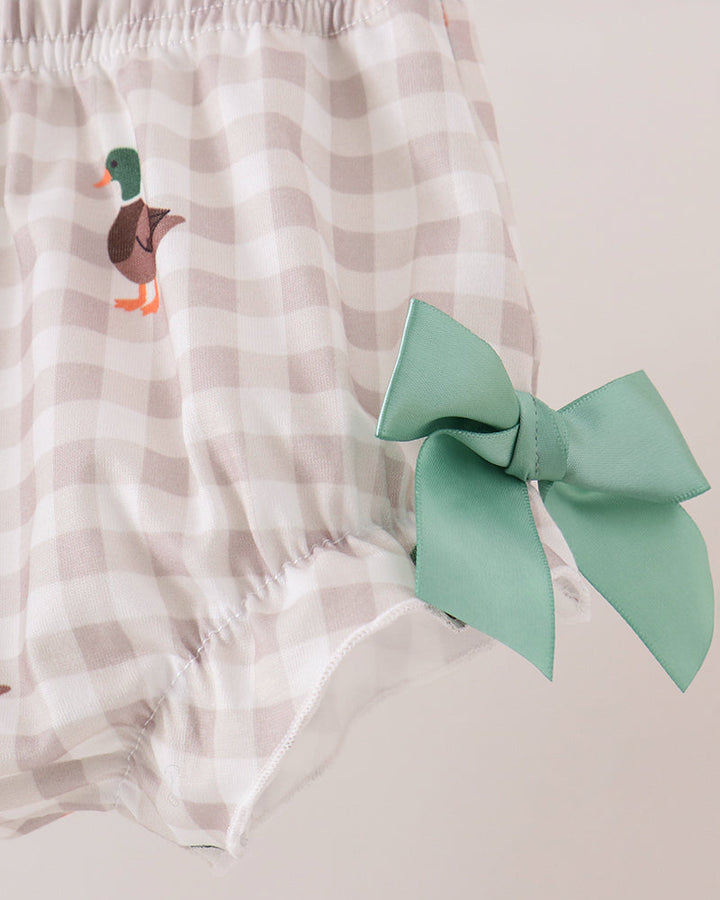 A close-up of a pair of baby bloomers with a beige and white gingham pattern, featuring a printed duck on the left leg and a large mint green bow on the right side.