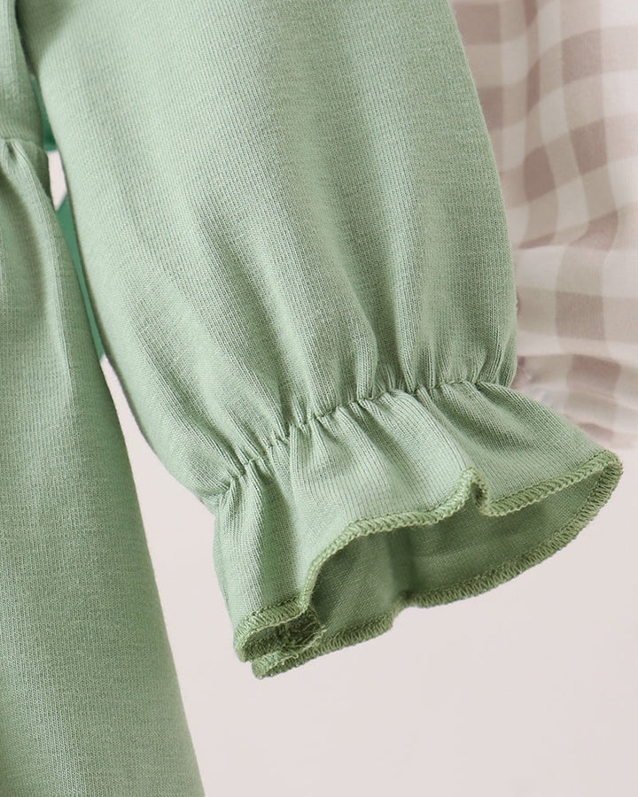 Close-up of a sage green long-sleeve blouse with a gathered ruffled cuff, shown against a soft light pink and white gingham background.