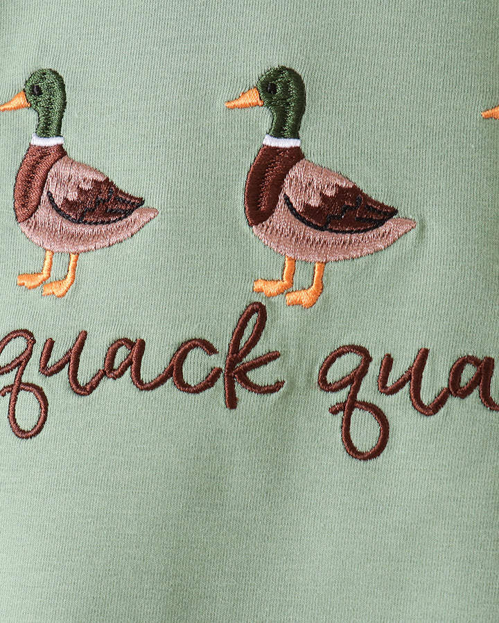 Close-up of a sage green embroidered fabric featuring two mallard ducks and the partial script text &