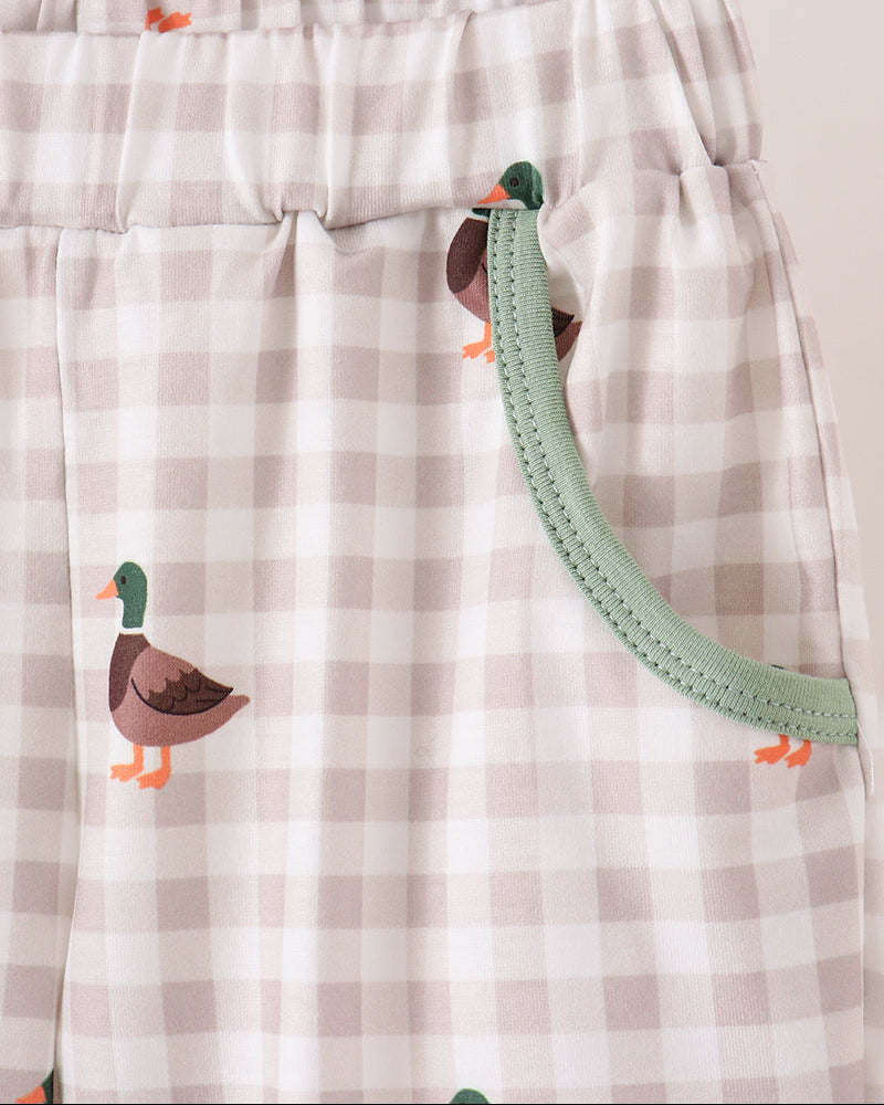 Close-up of a pair of baby pants with a beige and white gingham check pattern, featuring embroidered ducks and a mint green elastic waistband.