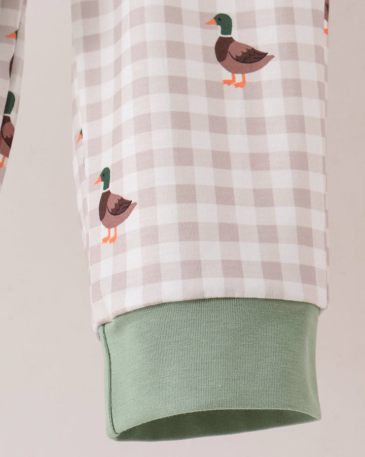 Close-up of a pajama sleeve with a beige and white gingham pattern, decorated with small duck illustrations, and finished with a sage green ribbed cuff.
