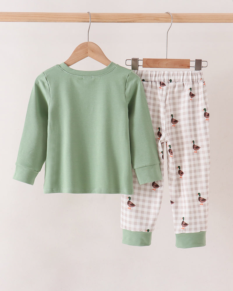 A two-piece pant set hanging on wooden hangers against a plain light beige wall. The set includes a sage green long-sleeve top and white gingham pants with a small duck print and sage green cuffs.