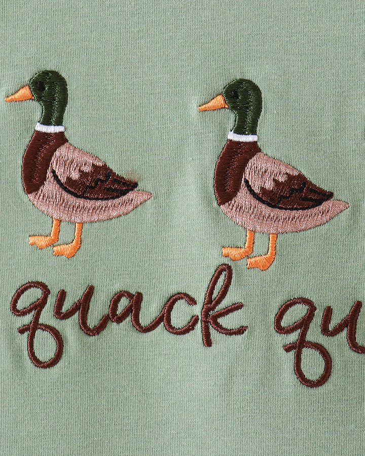 Close-up of embroidered ducks and the words "quack qu" on a sage green fabric surface.