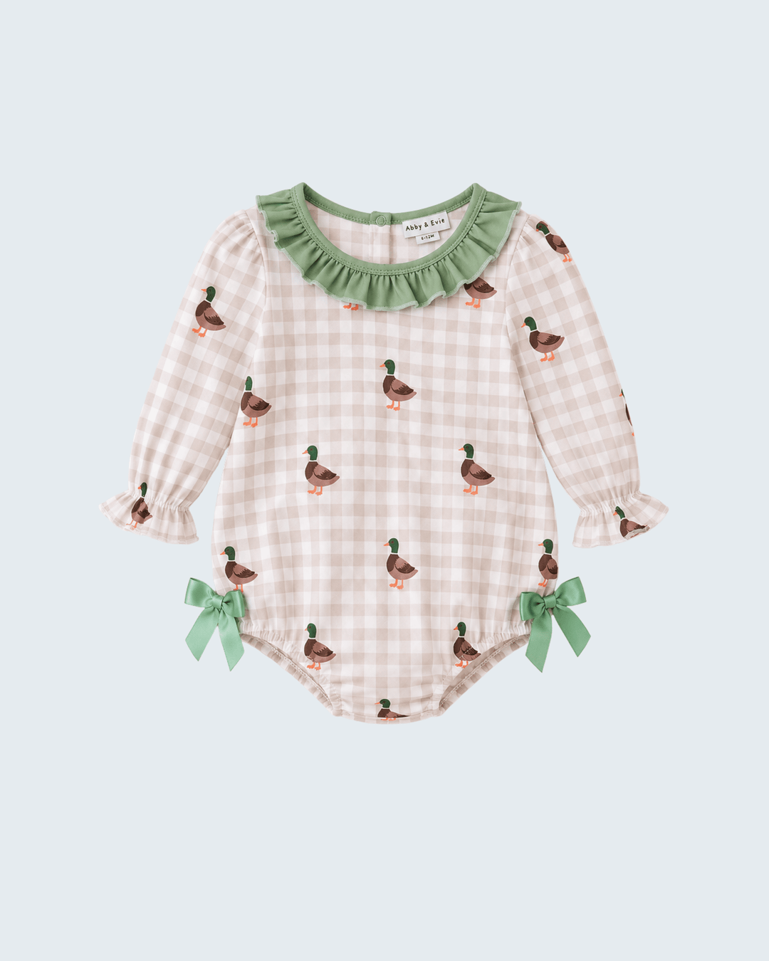 A baby long-sleeve romper in a light pink and white gingham pattern, decorated with small green and brown duck prints, a green ruffled collar, and green ribbon bows on the legs, shown against a light blue-gray background.