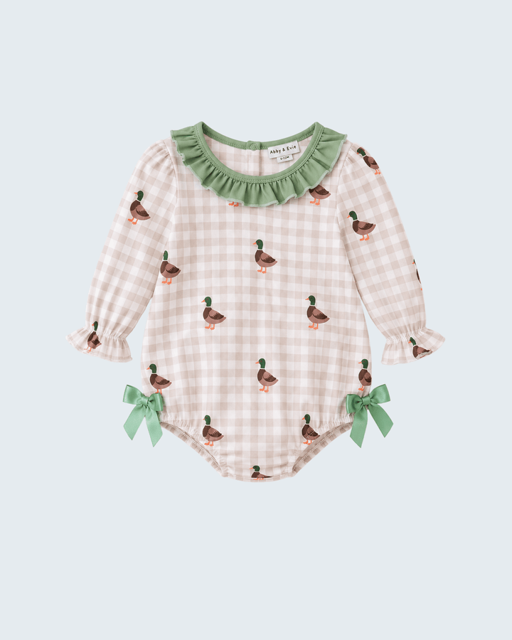 A baby long-sleeve romper in a light pink and white gingham pattern, decorated with small green and brown duck prints, a green ruffled collar, and green ribbon bows on the legs, shown against a light blue-gray background.