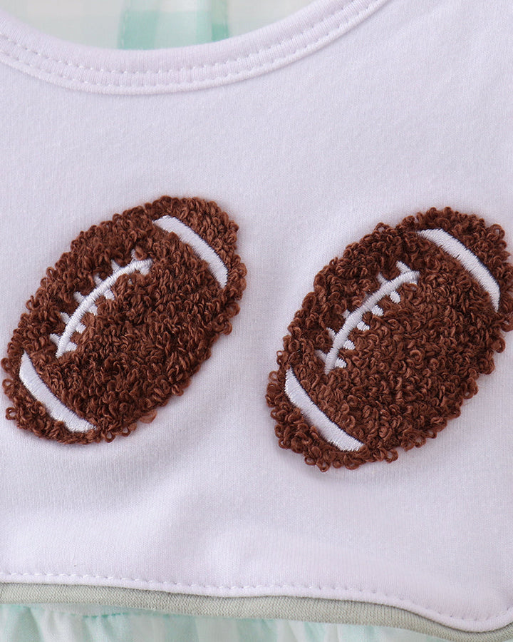 Close-up of a white baby top with two brown embroidered football appliqués on the chest and a small neck label reading Abby &amp; Co 6M.