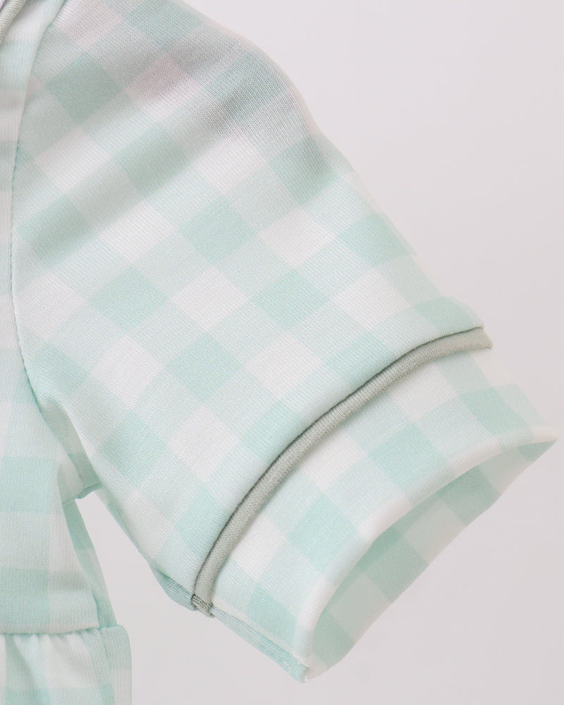 Close-up of a short-sleeve garment in a pale mint green and white gingham check pattern, showing the sleeve cuff with double stitching against a light gray background.
