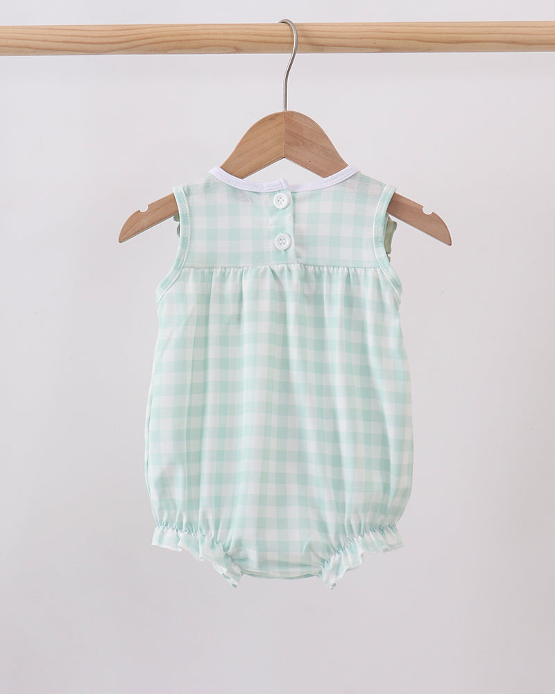 A baby romper in a light mint green and white gingham check pattern, hanging on a wooden hanger from a wooden clothes rack against a plain light gray wall.