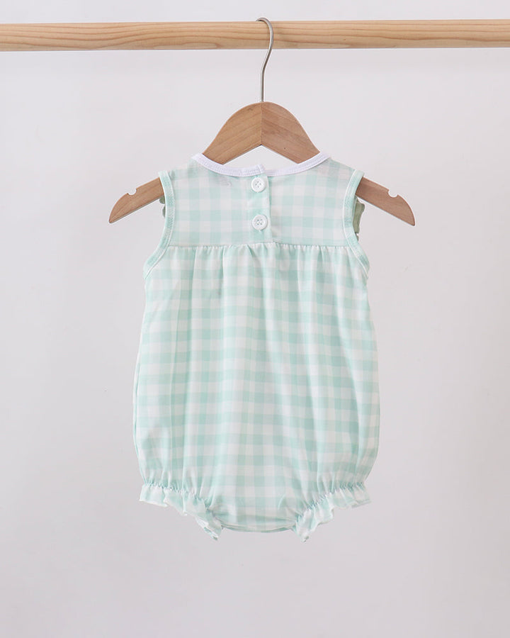A baby romper in a light mint green and white gingham check pattern, hanging on a wooden hanger from a wooden clothes rack against a plain light gray wall.