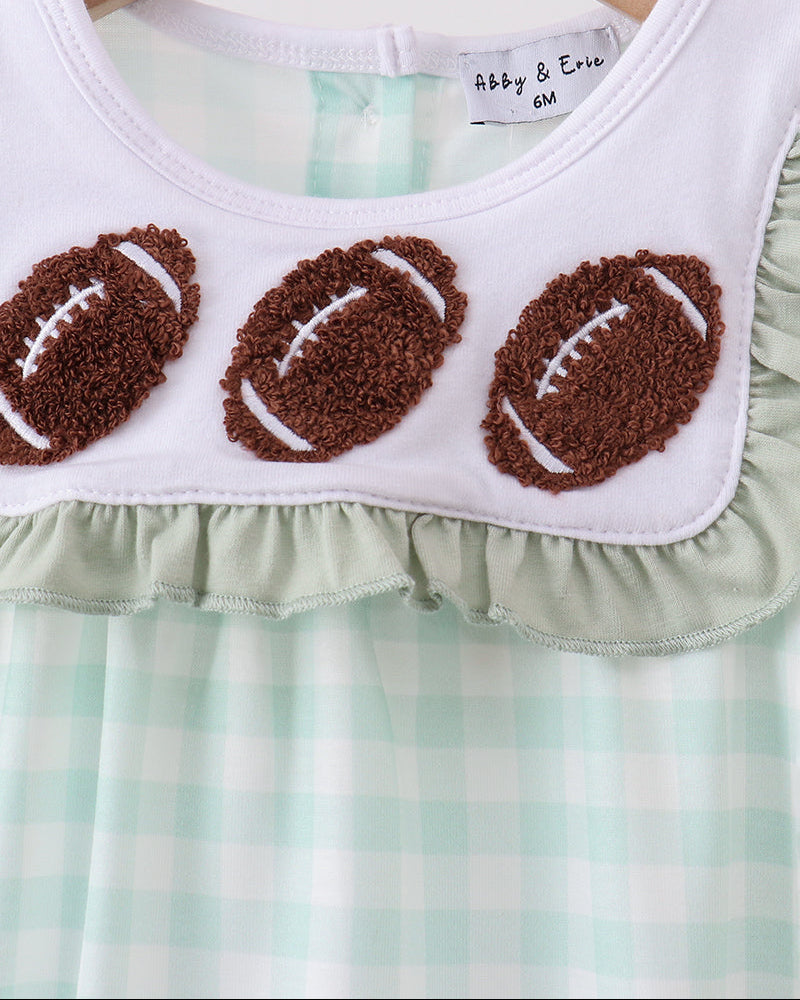 A close-up of a baby or toddler dress hanging on a wooden hanger. The top portion is white with three brown textured football appliqués outlined in white, and the lower portion is mint green and white gingham.