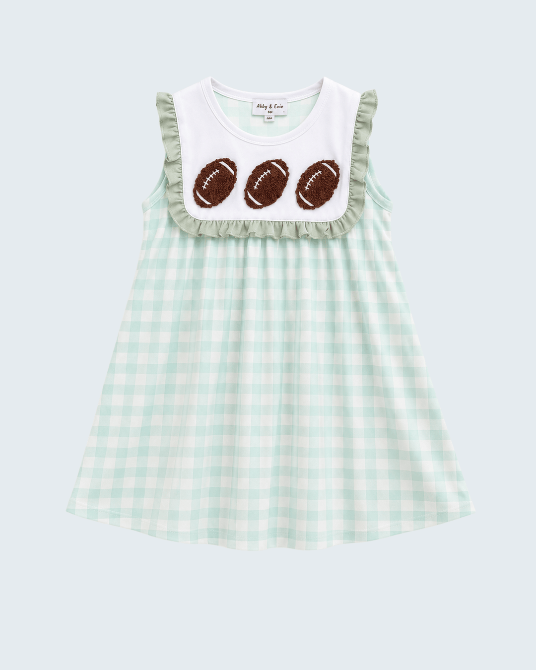 A sleeveless baby dress with a mint green and white gingham pattern, featuring a white bib-style yoke with ruffles and three brown football appliqués. The brand name &