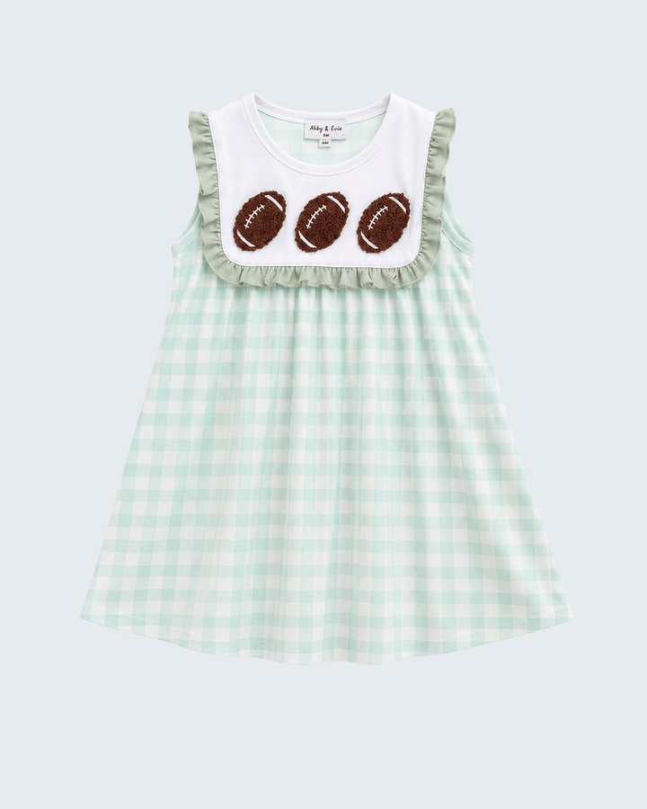 A sleeveless baby dress with a mint green and white gingham pattern, featuring a white bib-style yoke with ruffles and three brown football appliqués. The brand name &