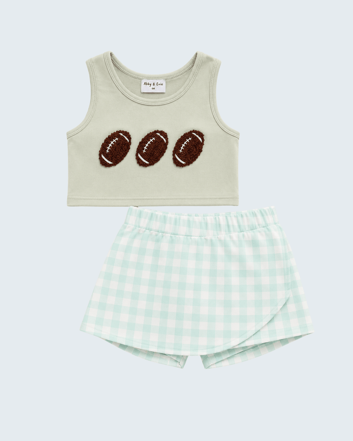 A two-piece baby outfit set featuring a light beige sleeveless crop top with three brown football patches, paired with mint green and white gingham shorts, shown on a light gray background.