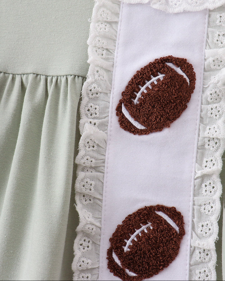 Close-up of a light sage green dress with a white vertical panel decorated with two brown football appliqués and white eyelet lace trim.