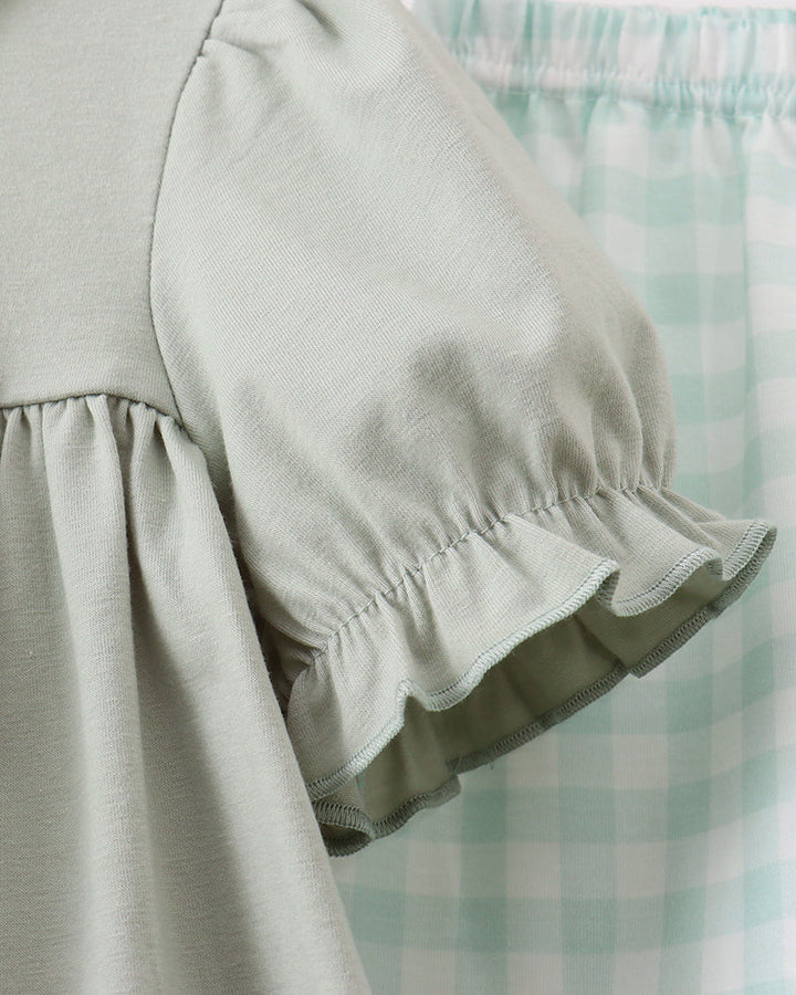 Close-up of a light sage green dress with a ruffled short sleeve, shown next to a mint green and white gingham skirt.