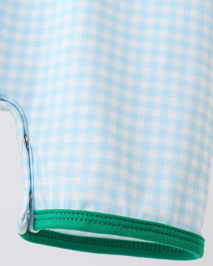 Close-up of a baby outfit with blue and white checkered pattern and green trim on a white background