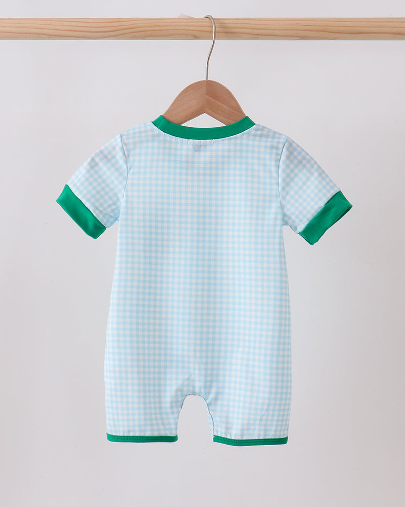 Baby romper with green trim hanging on a wooden hanger against a light background