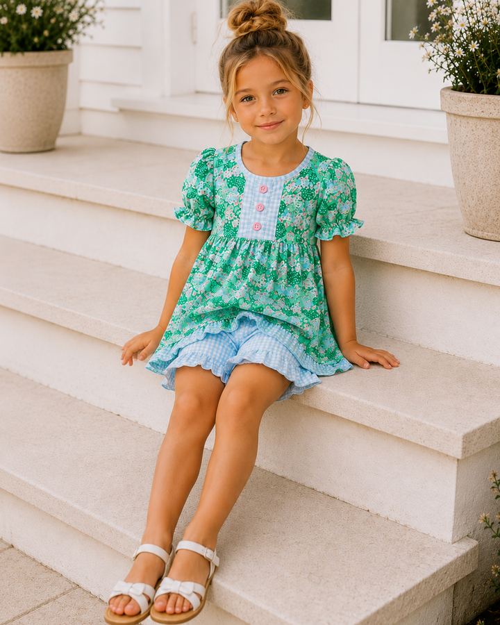 Young girl in a green floral dress sitting on white steps.