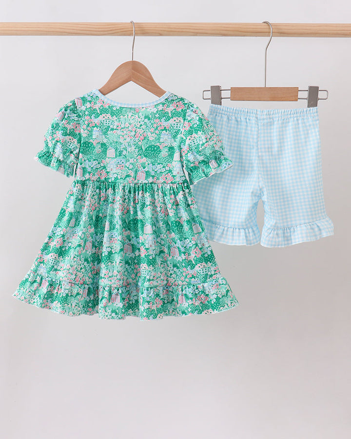 Green floral dress and blue checkered shorts on hangers against a white background