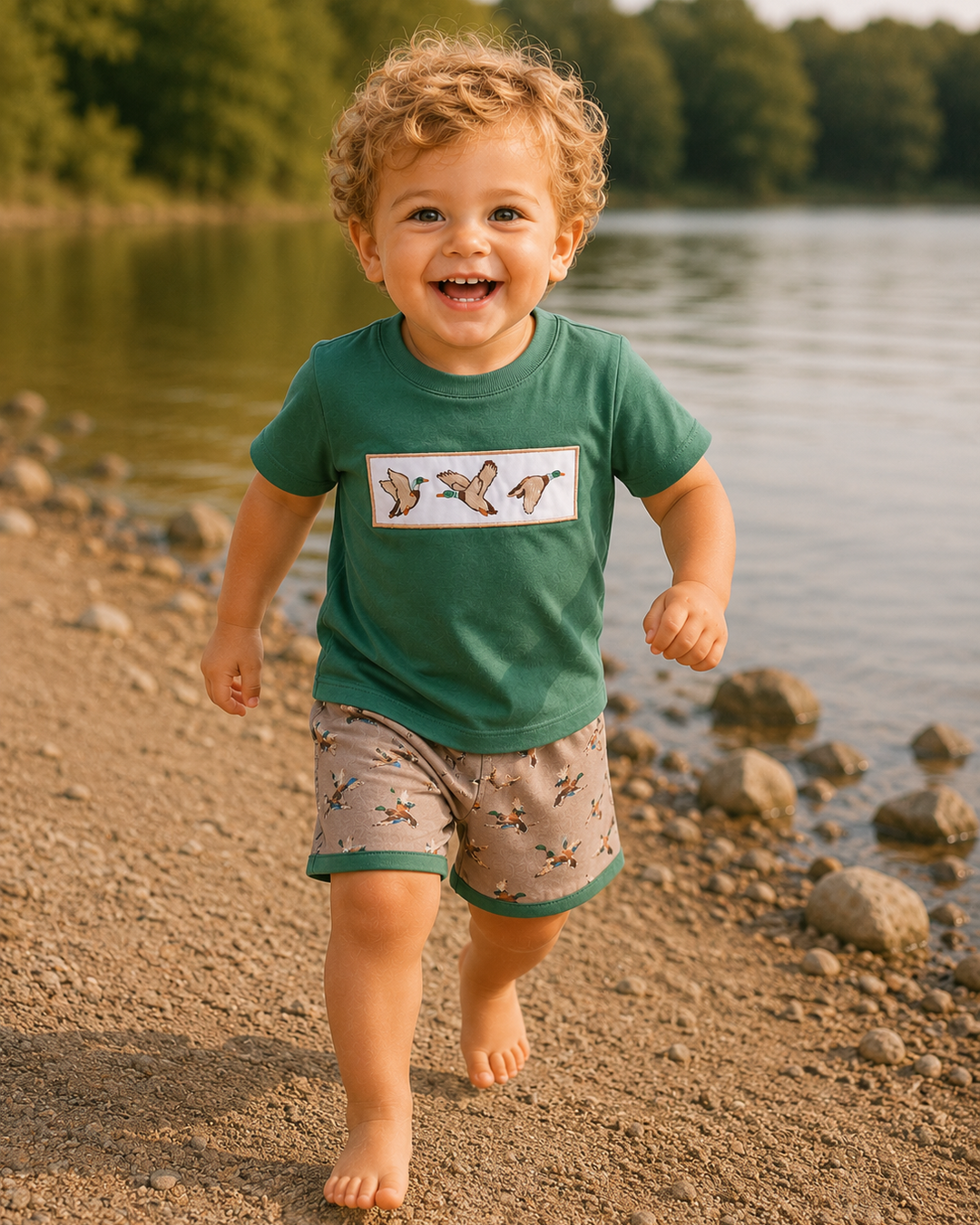Child in a green shirt and patterned shorts running on a rocky beach with trees in the background