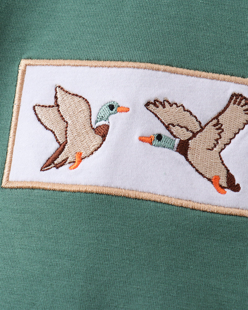 Embroidered design of two ducks on a green fabric background
