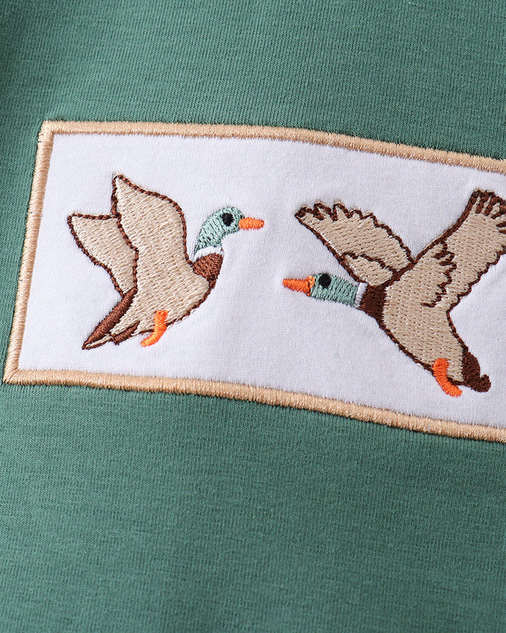 Embroidered design of two ducks on a green fabric background