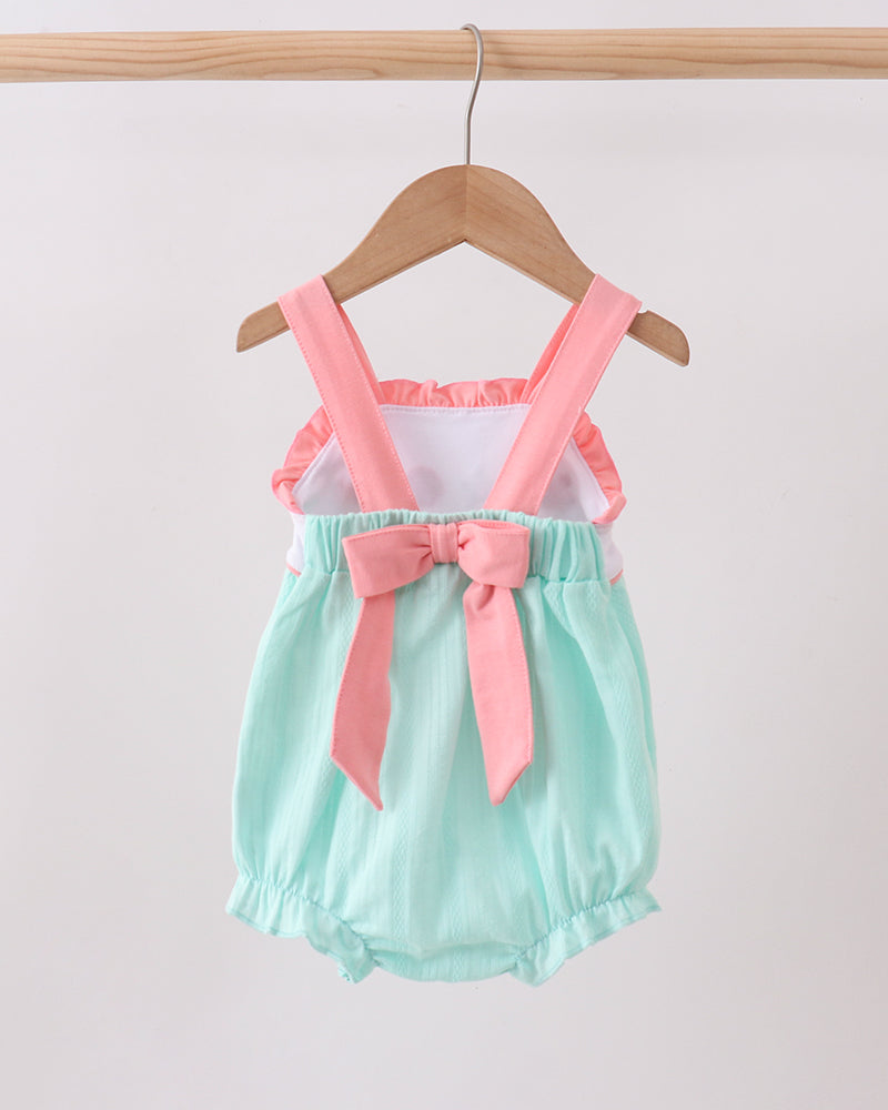 Mint green romper with pink suspenders and bow on a wooden hanger against a white background