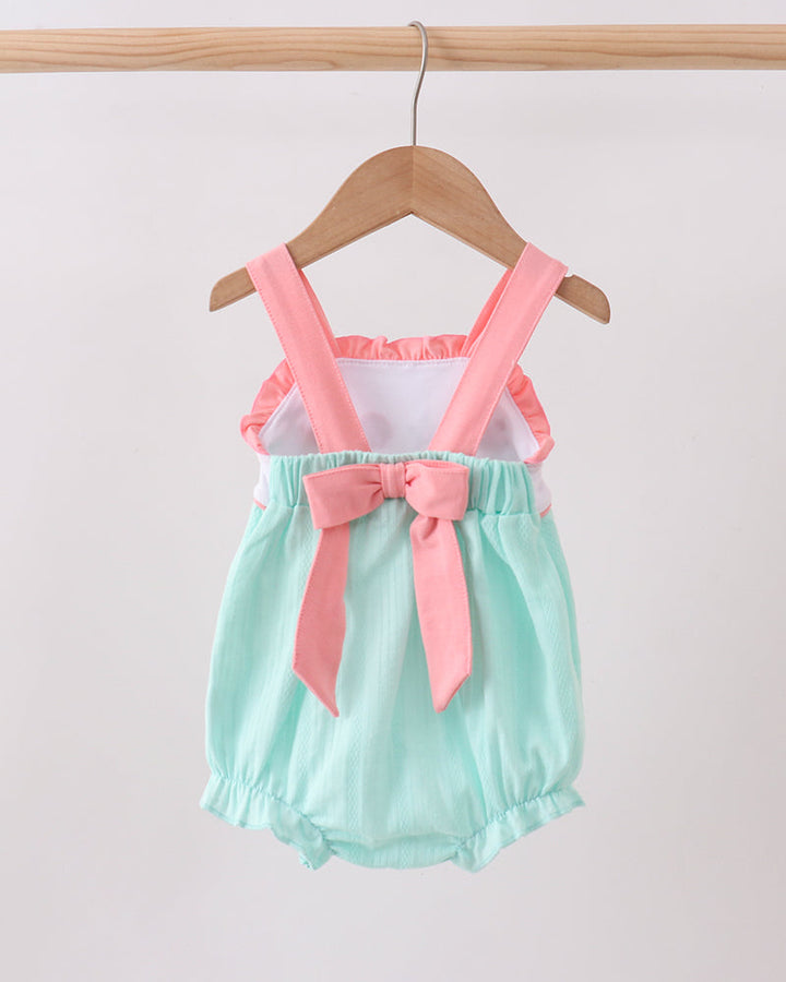 Mint green romper with pink suspenders and bow on a wooden hanger against a white background