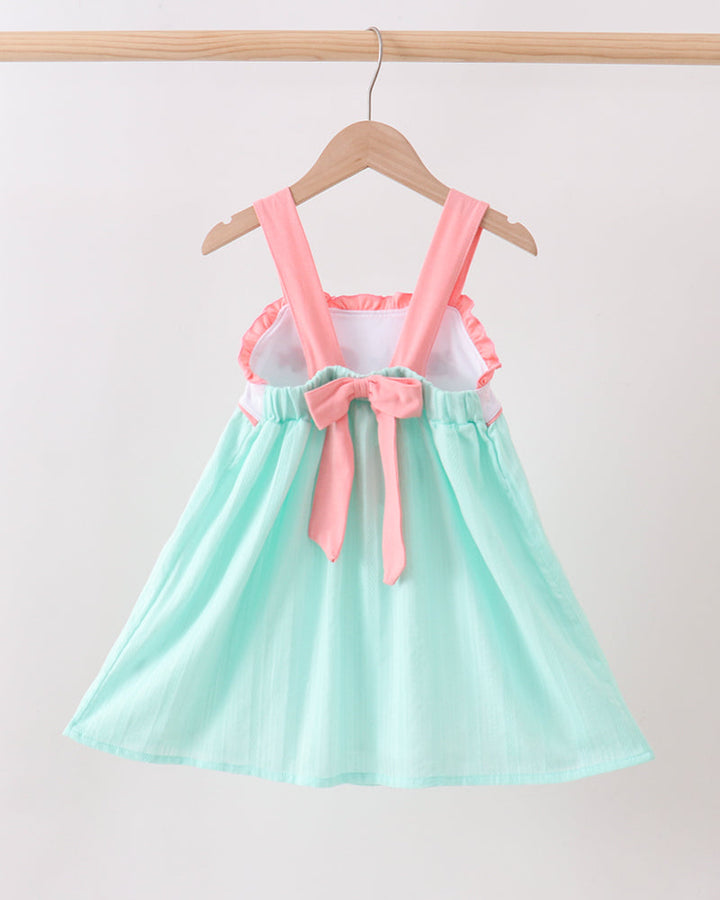 Mint green dress with pink suspenders and bow on a hanger against a white background