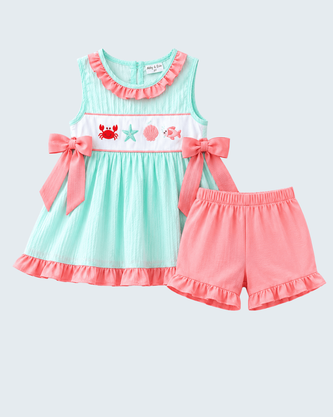 Children's outfit with a turquoise dress and pink shorts on a light gray background