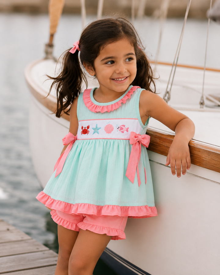 Young girl in a light blue and pink dress with a sailboat in the background