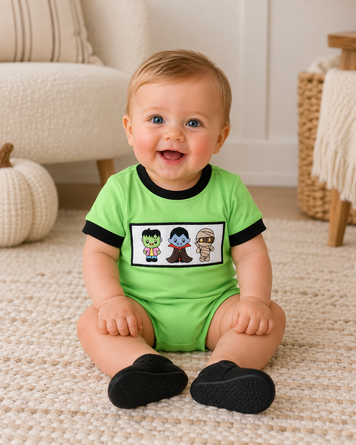 Green bubble romper with black trim and embroidered monster character patch