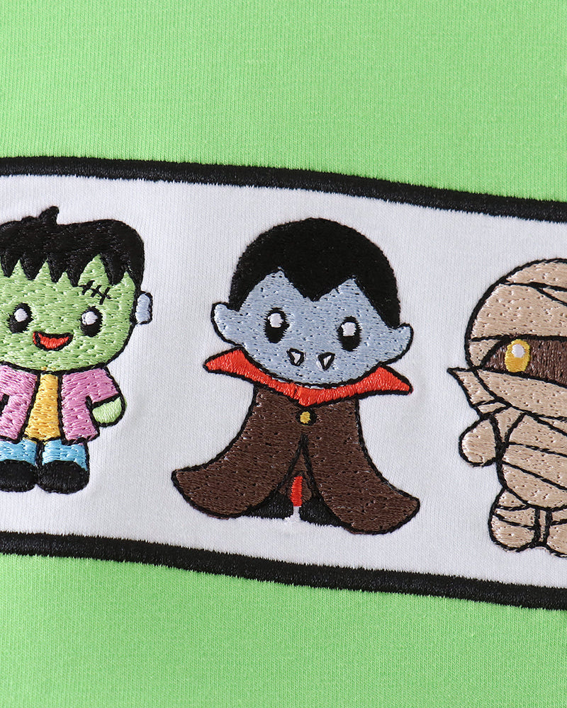Green romper with black-trimmed band and embroidered cartoon characters