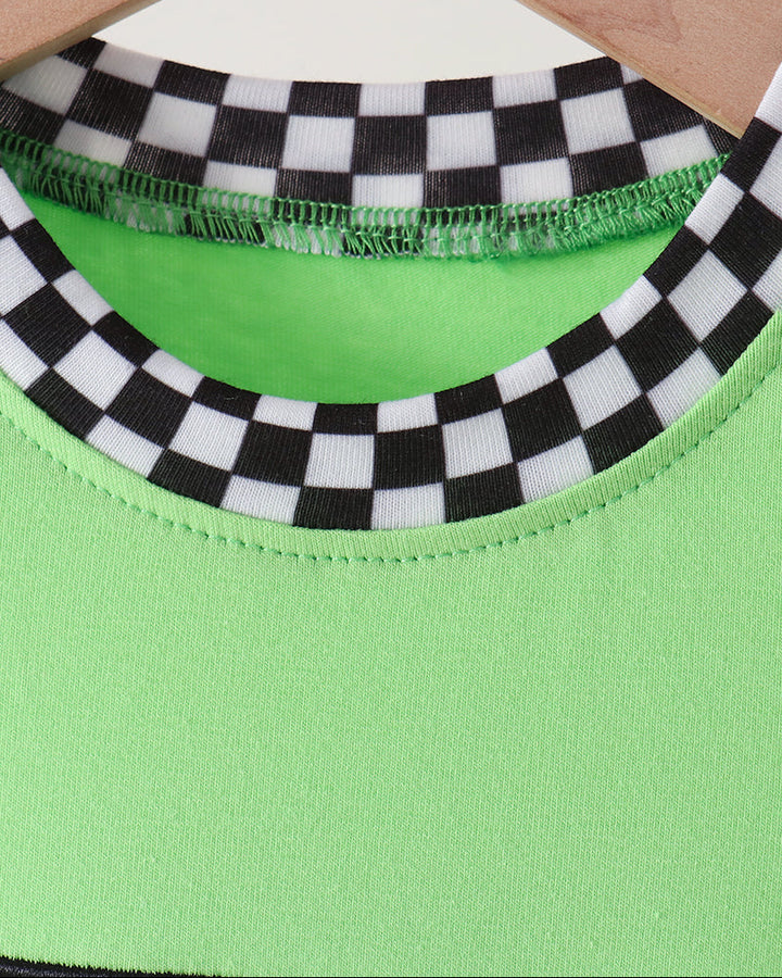 Close-up of a bright neon green top on a wooden hanger, featuring a black and white checkered trim around the crew neckline.