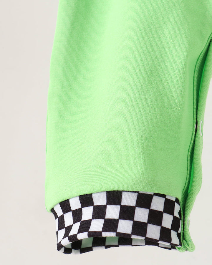 Close-up of a bright neon green garment sleeve or leg with a black-and-white checkered fabric cuff, shown against a plain light background.