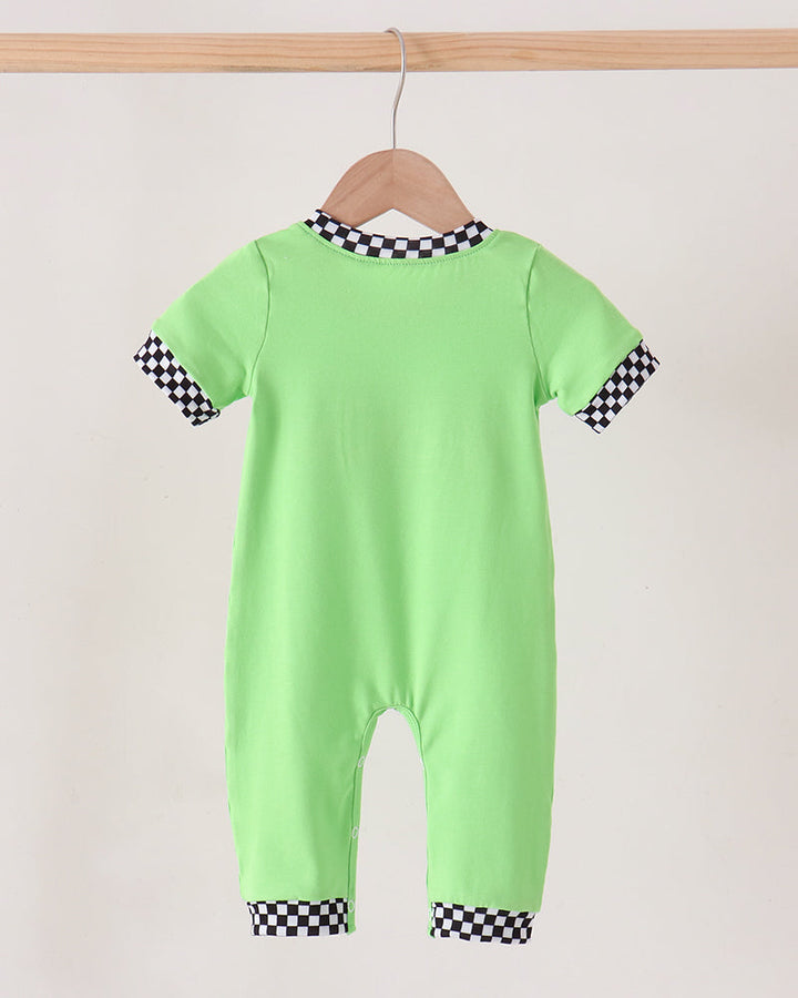 A neon green baby jumpsuit hanging on a wooden hanger against a plain off-white wall. The jumpsuit features black and white checkered trim at the collar, sleeve cuffs, and ankle cuffs.