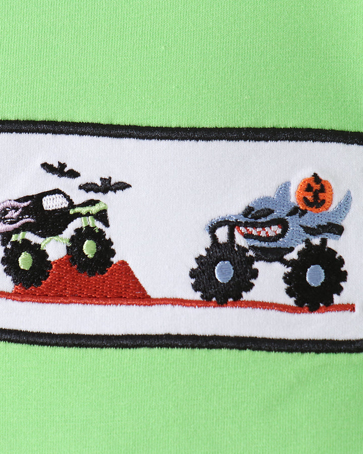 Close-up of a bright lime green garment featuring a horizontal embroidered band with monster trucks, bats, and a jack-o&